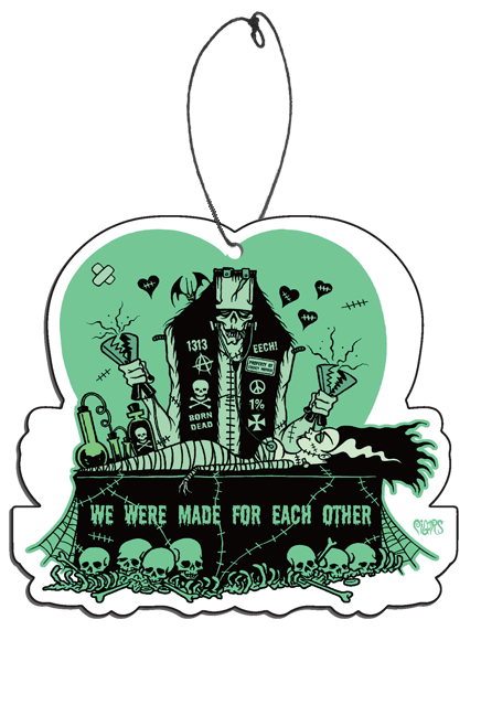 Air freshener.  Pale green heart background.  Frankenstein like monster holding jumper cable clamps, standing over bride of frankenstein-like woman, lying on black coffin surrounded by green bones and skulls.  Green text on coffin reads we were made for each other.