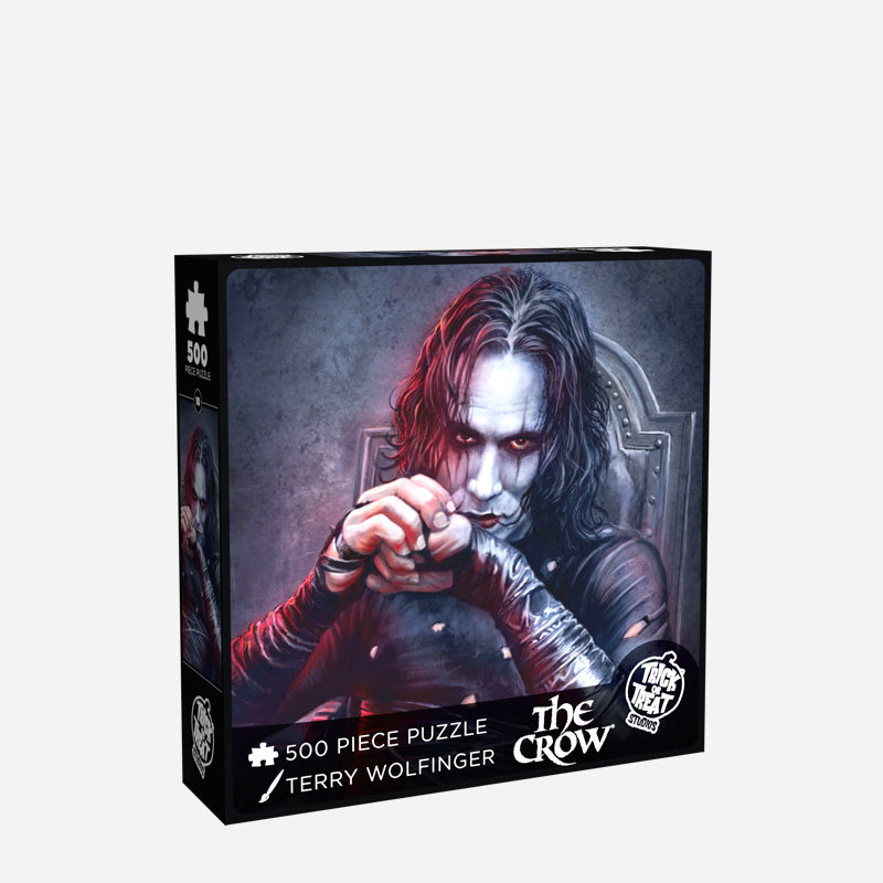 Product packaging. Cover. Black box, white text reads 500 piece puzzle, Terry Wolfinger, The Crow, white Trick or Treat Studios logo. Illustration of Brandon Lee as the Crow, black and white background, upper body of a dark haired man with a pale white face and eye makeup, wearing tattered black skin-tight clothing, sitting in a gray chair.