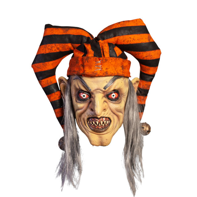 Mask, front view. Long, straight gray hair, high gray eyebrows. Large ears. Black-rimmed bloodshot eyes, pale irises. Mouth in evil grin, pink gums dirty sharp teeth, gray lips. Wearing dirty orange and black striped jester hat with bells on ends.