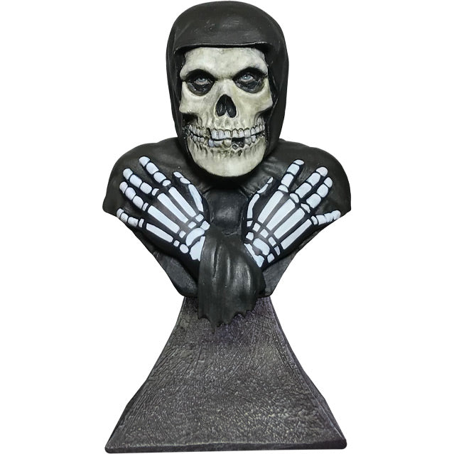 Mini bust, front view. Head, shoulders and upper chest. Misfits Fiend, skeleton face and hands, crossed, wearing black hooded cloak.  Set on gray stone textured base.