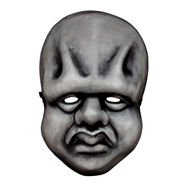 Plastic face mask, front view. Black and white toned.  Bald, vertical ridges in forehead, heavy brow, bags under eyes, bulbous nose, full cheeks, large lips. 