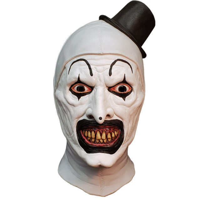 Mask, head and neck, front view. Evil grinning, black and white clown face, high black painted eyebrows, black around eyes and mouth, black dot on tip of nose, pink gums and yellow teeth. wearing tiny black top hat.