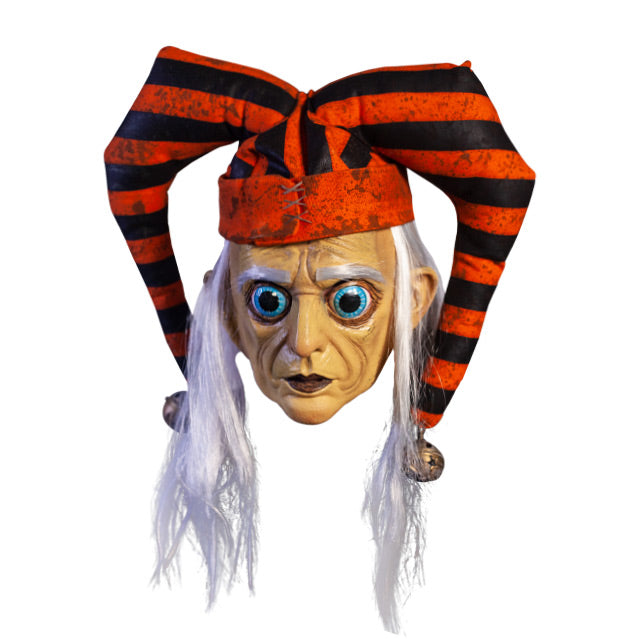 Mask, front view. Long, straight white hair, white eyebrows. Large ears. Large round blue eyes with very large pupils. Mouth closed, dark lips. Wearing dirty orange and black striped jester hat with bells on ends.