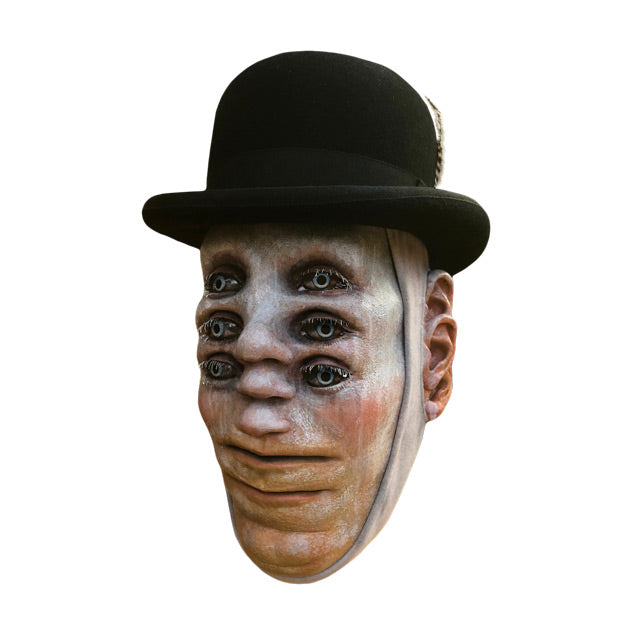 Mask.  Wearing Bowler hat.  Pale white skin.  3 sets of blue eyes one above the other, 3 noses one above the other in center of face, two mouths, one above the other at bottom of face, 3 ears on each side of head.