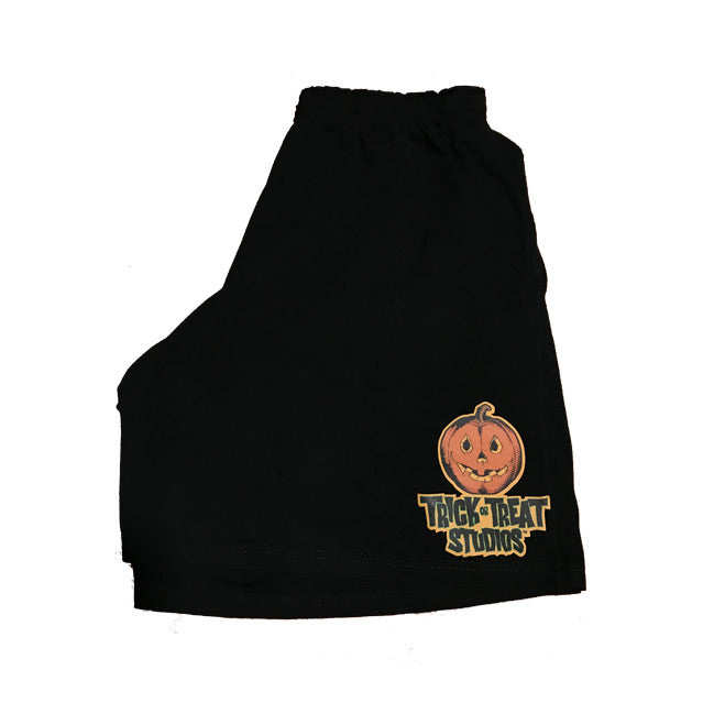 Black shorts. Logo on left leg. Orange yellow and black Jack o' lantern with smiling mouth, above black text that reads Trick or Treat Studios. 