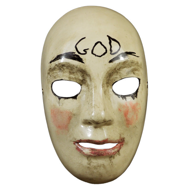 Plastic face mask, front view. Pale tan, dirty nondescript face, holes for eyes and mouth. Black lined eyeholes, painted on black eyebrows. Smeared pink blush on cheeks, pink on lips. Handwritten black text on forehead reads GOD