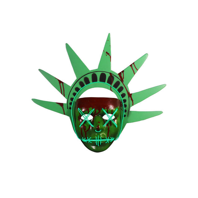 Plastic face mask. Front view.  Green mask with nondescript facial features, bloodstains on forehead dripping down face and on green Lady Liberty headpiece. Light up strands of wire threaded around bottom edge of headband, across eyes in an x, in a semicircle under nose, and stitched across mouth. 
