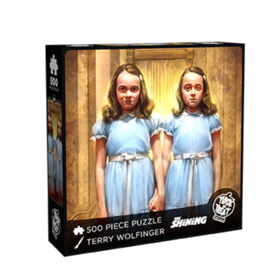 Product packaging. Cover. Black box, white text reads 500 piece puzzle, Terry Wolfinger, The Shining,  white Trick or Treat Studios logo. Illustration of two identical girls holding hands, light brown hair, white barrette on right side of their heads, blue dresses with ruffled shoulders, pink ribbon at their waists.  brown background