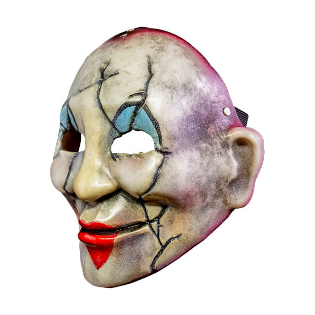 Injection plastic face mask, left side view. Distressed and dirty white face, red around edges, cracks around eyes, cheeks and left side of mouth, blue and black painted clown eyelids, red heart painted over lips of smiling mouth.