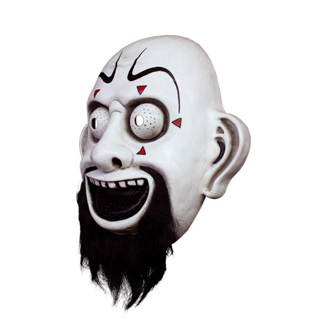 Vacuform plastic face mask, left side view. Bald clown-like face, exaggerated drawn black eyebrows, small red triangles around large white eyes, large ears, Black grinnig mouth showing top teeth, full black beard