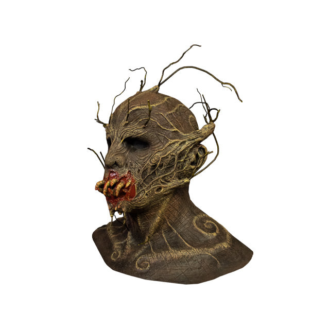 Mask, left view. Head neck and collarbones. Creature, brown woody bark-like flesh, twigs coming from top of head, eyebrows, upper cheekbones, jaw and chin. Gory mouth with yellow worm-like teeth.