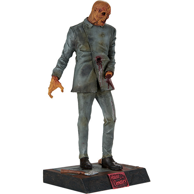 Statue, right side view. Zombie figure, orange hued decaying flesh, wearing distressed, dirty, bloodied blue doctor's coat and blue pants, black shoes, missing left hand. Standing on black, dirty base, severed hand and hatchet are resting on base, plaque on front red text reads house by the Cemetary.