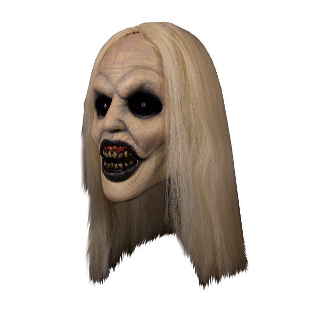 Mask, left view. Long, straight blond hair, pale skin, veins showing through. Large empty black eyes. Mouth open showing dark red gums dirty yellow teeth, black lips.