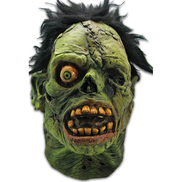 Mask,  front view. Black bushy hair, Green flesh, wrinkled and wounded. Bulging, bloodshot right eye, missing left eye and nose. Open snarling mouth with yellow crooked teeth.