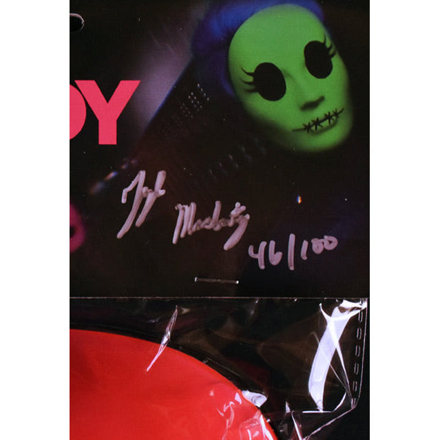 Product packaging. Black with image of green facemask, top of pink mask shown. Signature and number of limited edition.