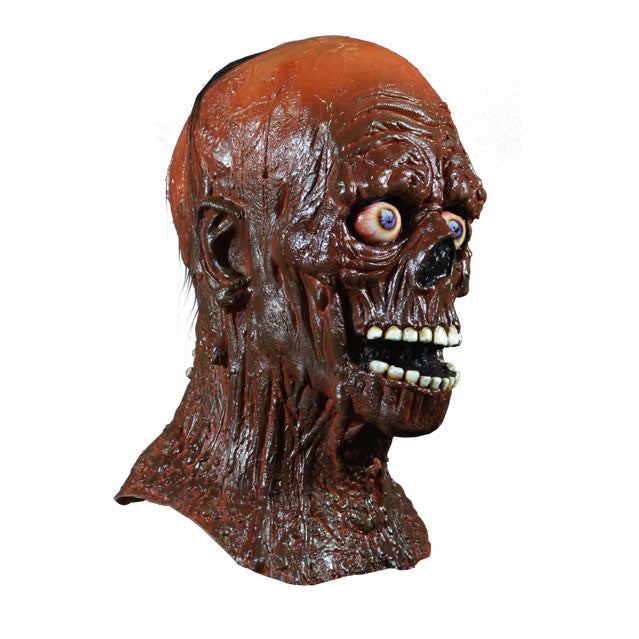 Mask, head and neck, right side view. Tarman, skeletal face, sparse hair, covered in brown tar. Blue, bloodshot eyes. Mouth open, many white teeth