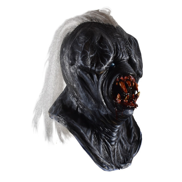 Mask, right side view. head, neck and upper chest. Long white hair in center of head. Black skin, wrinkled, nearly nonexistent eyes and nose. Large round gory mouth with sharp bloody teeth.