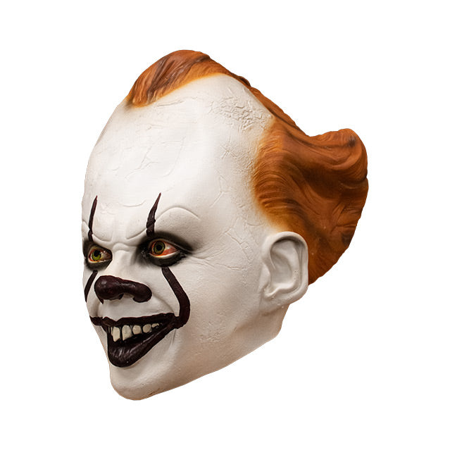 Mask, left side view. IT clown face, red hair, white skin, large forehead, Dark red nose, dark lips, creepy smile with crooked buck teeth.