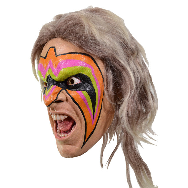 Mask, left view. Long ash blond hair. Angry male face, mouth open in a yel showing teeth and tongue. Orange, pink, bright green, and black face paint on forehead, eyes, nose and cheeks.