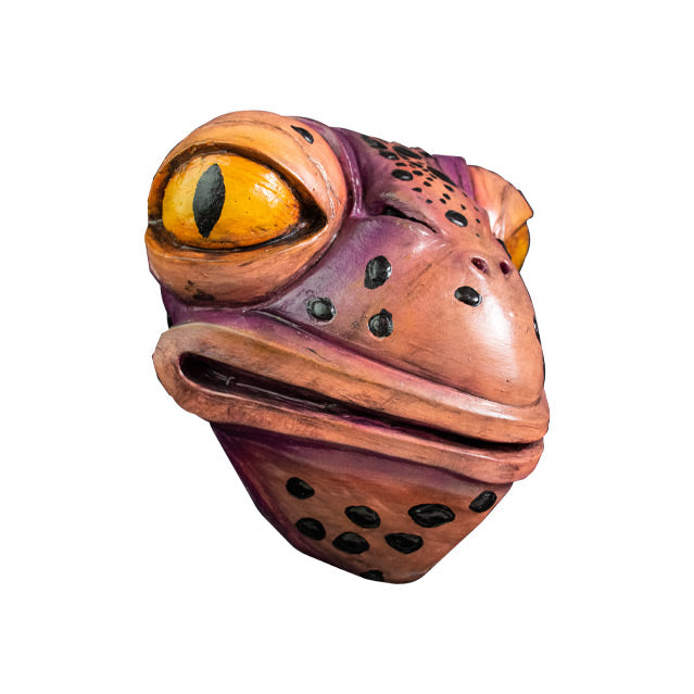 Mask, right view. Pale pink and purple toad face with black spots, large yellow eyes, 2 small nose holes between eyes. Large, wide mouth and neck.