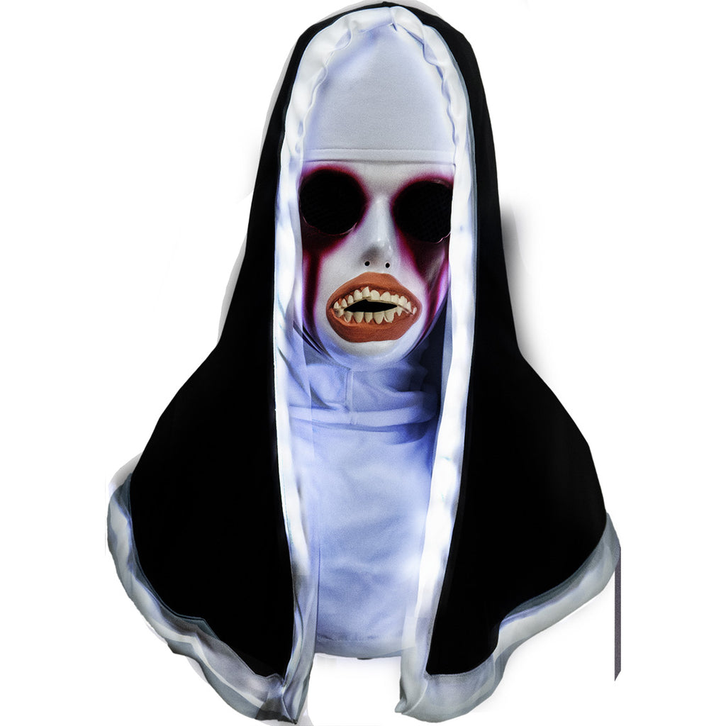 Plastic face mask and nun habit, head, neck and shoulders. Front view, LED lights in white trim lit. White face, large black mesh covered eye holes, painted in dark red around eyes and dripping down face. Distorted mouth with large peach-colored lips, large crooked teeth. Wearing white trimmed black nun's habit over white head covering and shirt top