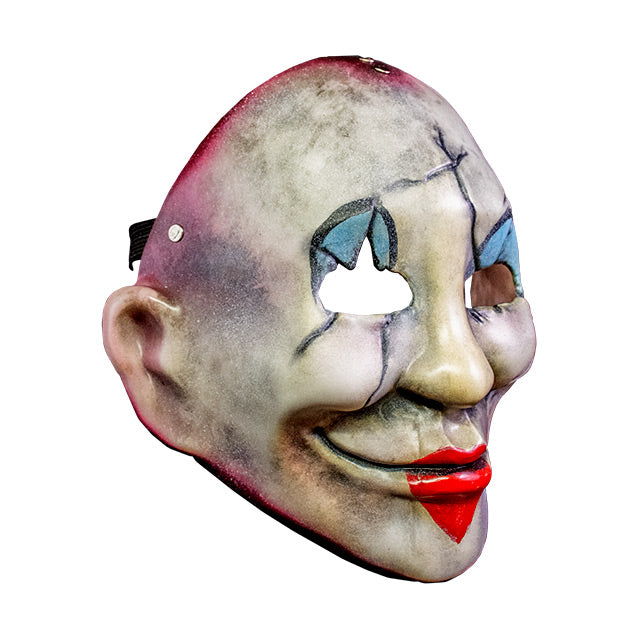 Injection plastic face mask, right side view. Distressed and dirty white face, red around edges, cracks around eyes, cheeks and left side of mouth, blue and black painted clown eyelids, red heart painted over lips of smiling mouth.