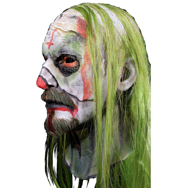 Mask, head and neck, left side view. Long, stringy greenish-blond hair. white painted skin, pale red inverted cross on forehead, pale red around eyes surrounded by black circles. Pale red on tip of nose, around mouth down chin and onto neck. moustache and goatee.