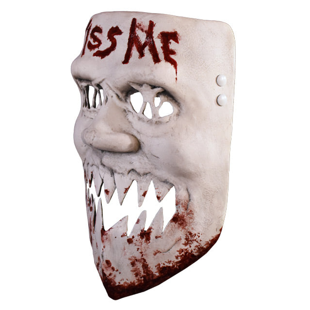Plastic face mask, left view. White distressed finish, blood stains on chin, Large nose, mouth open jagged cut out teeth. Text written in blood on forehead reads kiss me.