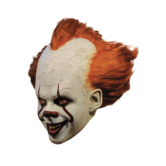 Mask, left side view. IT clown face, red hair, white cracked skin, large forehead, red eyes and nose, dark lips, creepy smile with crooked buck teeth.