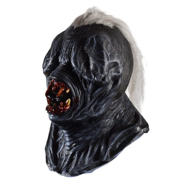 Mask, left side view, head, neck and upper chest. Long white hair in center of head. Black skin, wrinkled, nearly nonexistent eyes and nose. Large round gory mouth with sharp bloody teeth.