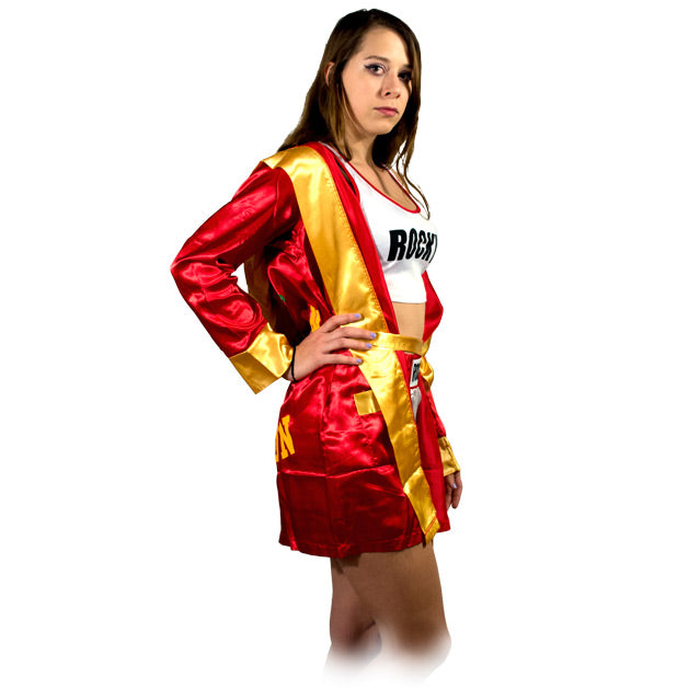Side view, woman wearing short, hooded, red satin robe, gold trim and cuffs. over white and orange boxing trunks. White tank top red trim, black text reads Rocky.