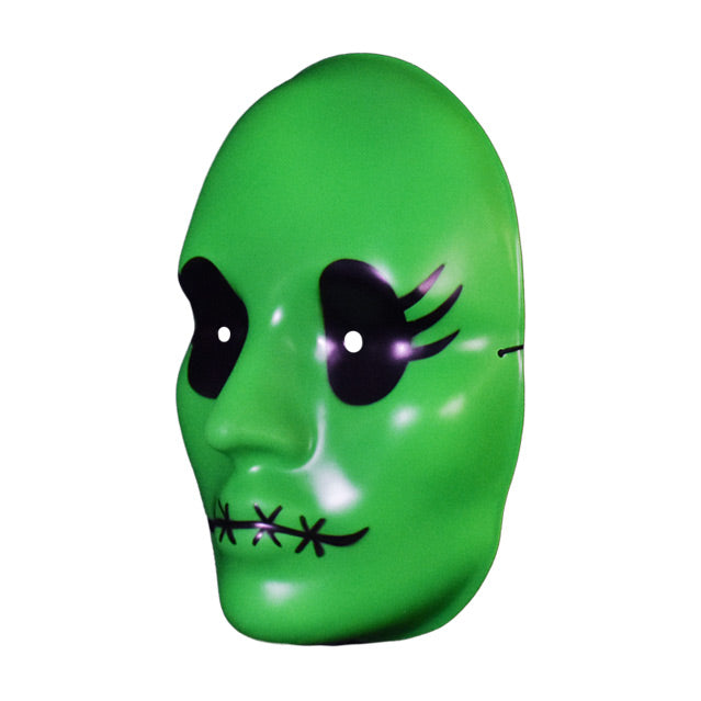 Vacuform plastic face mask, left view. Bright green face, large black eyes with 3 eyelashes on the sides, 4 black x stitches across lips.