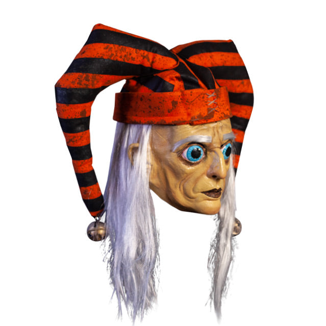 Mask, right view. Long, straight white hair, white eyebrows. Large ears. Large round blue eyes with very large pupils. Mouth closed, dark lips. Wearing dirty orange and black striped jester hat with bells on ends.