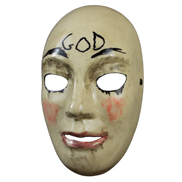 Plastic face mask, left view. Pale tan, dirty nondescript face, holes for eyes and mouth. Black lined eyeholes, painted on black eyebrows. Smeared pink blush on cheeks, pink on lips. Handwritten black text on forehead reads GOD