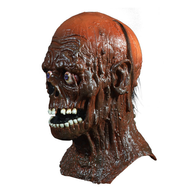Mask, head and neck, left side view. Tarman, skeletal face, sparse hair, covered in brown tar. Blue, bloodshot eyes. Mouth open, many white teeth