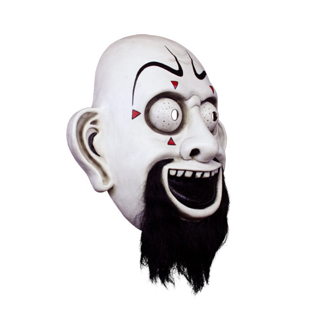Vacuform plastic face mask, right side view. Bald clown-like face, exaggerated drawn black eyebrows, small red triangles around large white eyes, large ears, Black grinnig mouth showing top teeth, full black beard