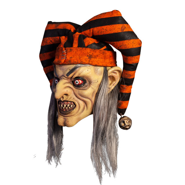 Mask, left view. Long, straight gray hair, high gray eyebrows. Large ears. Black-rimmed bloodshot eyes, pale irises. Mouth in evil grin, pink gums dirty sharp teeth, gray lips. Wearing dirty orange and black striped jester hat with bells on ends.