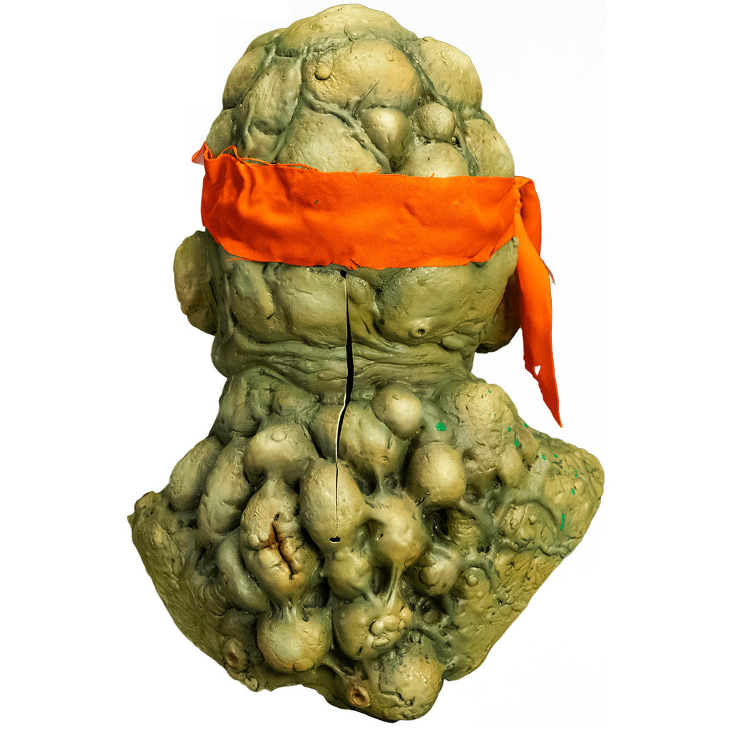 Mask, head, neck and upper chest. back view. Green lumpy blistered flesh, bald with bright orange headband tied around forehead. Bumpy neck and back with sores.