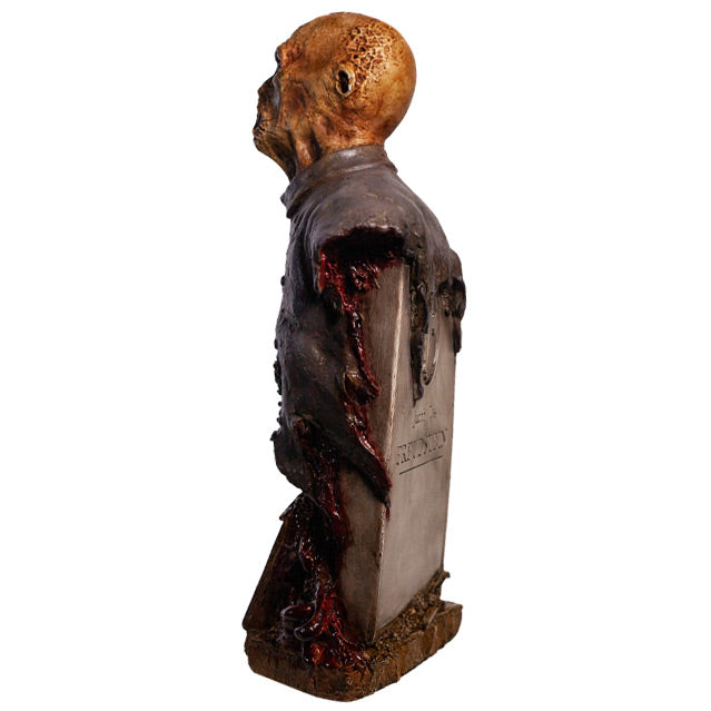 Zombie bust, left side back view, head, shoulders and chest. Orange-hued shriveled flesh, wearing filthy and gory blue doctor's coat. Gore coming from bottom of torso. Gray tombstone in back, set on wood look base.