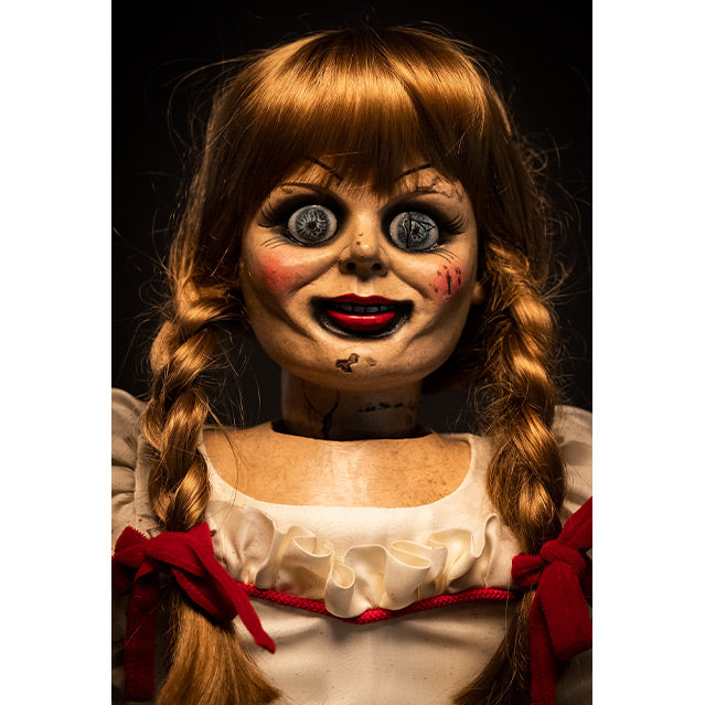 Doll, close up of head and chest, front view, black background. Large blue eyes, distressed finish on face. Blond hair with bangs, two braids tied with red ribbon. White dress with red trim at chest.  