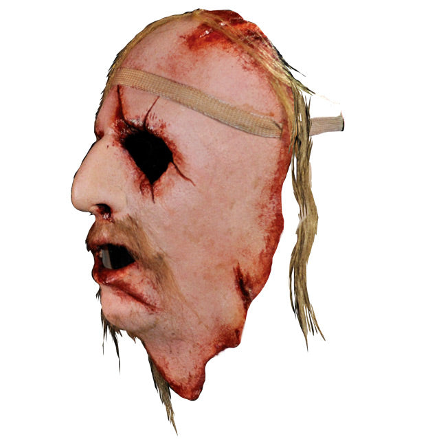 Face Mask, face and neck, left side view. Man's face, bloody with cuts and wounds around forehead, eyes, nose , mouth and neck. Sparse locks of blond hair, long blond moustache. Bandage around forehead.