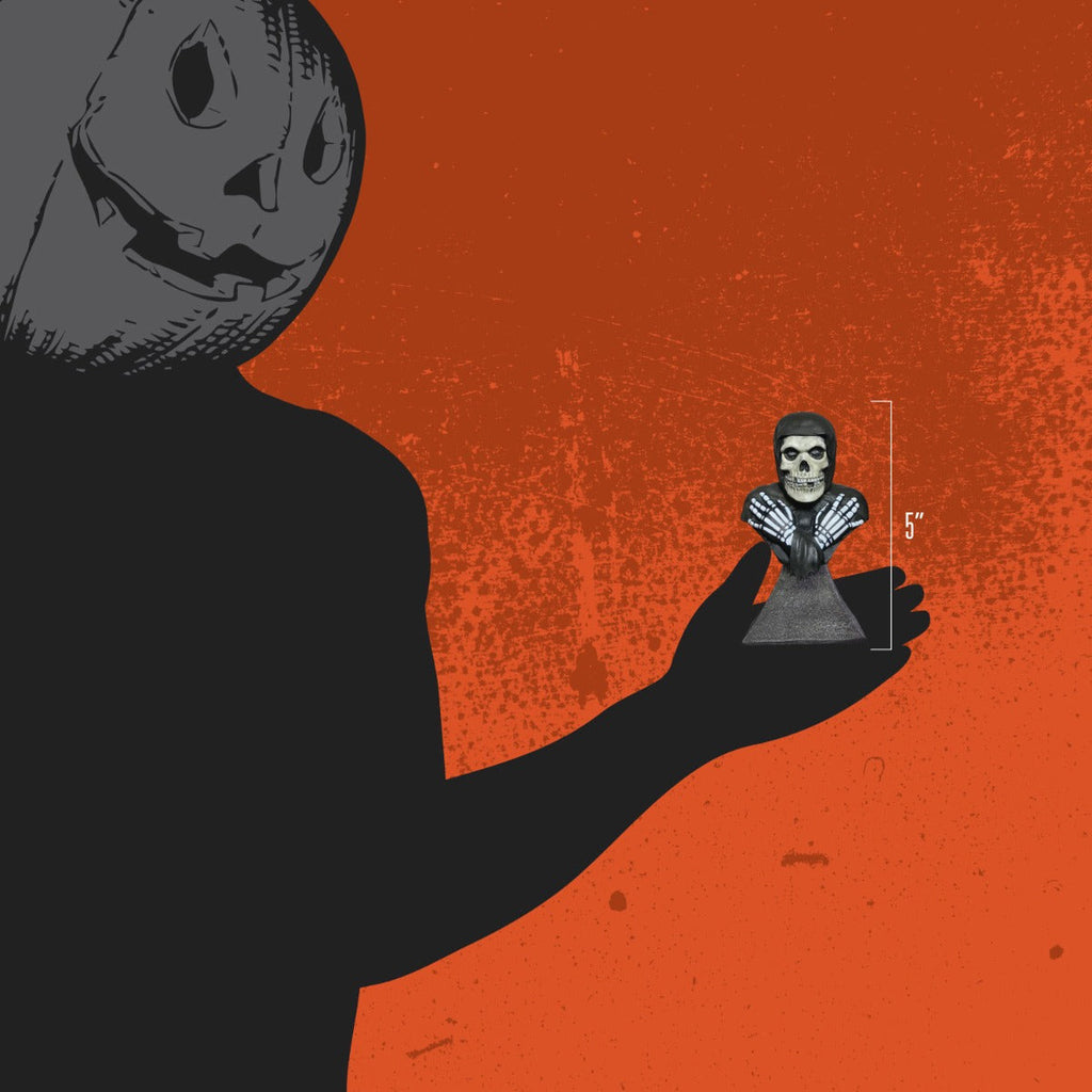 Orange background.  Person wearing black, jack o' lantern head, holding mini bust to show size, 5 inches