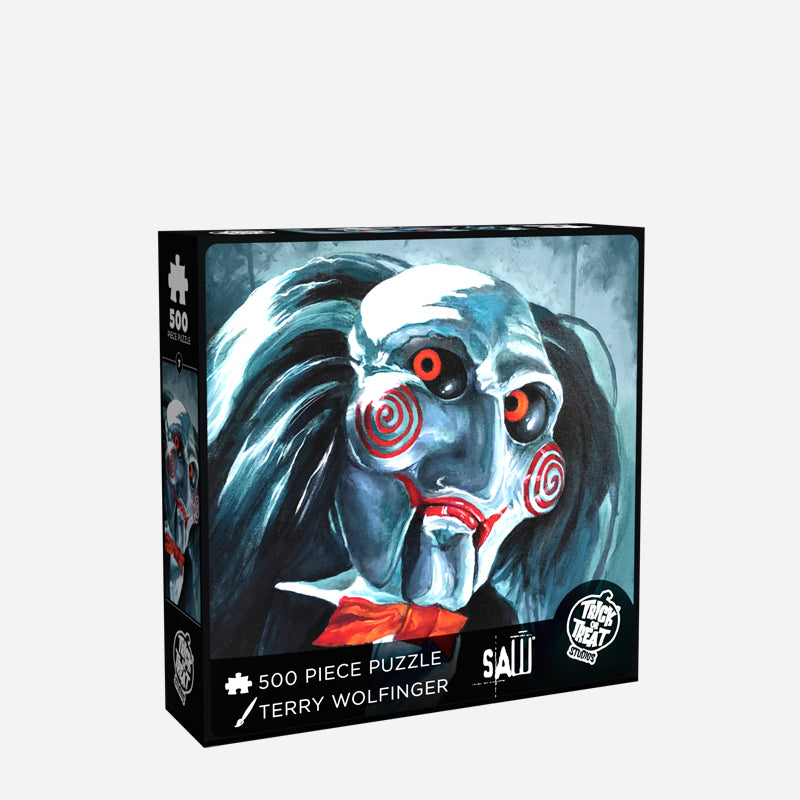 Product packaging. Cover. Black box, white text reads 500 piece puzzle, Terry Wolfinger, SAW, white Trick or Treat Studios logo. Illustration of the Saw Billy puppet head and shoulders, black and white background, balding with black hair, white face, black-rimmed red eyes, red spirals on cheeks, red lips on hinged ventriloquist dummy mouth. Wearing red bowtie, white collared shirt, black vest and suit coat. 