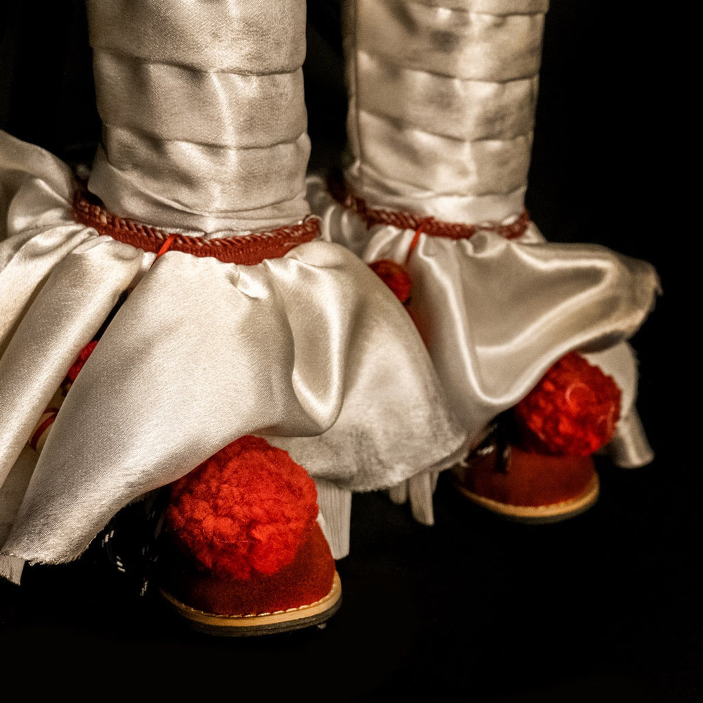 Close up of costume shoes, bottom pants ruffle, red trim, red shoes with red pompoms.