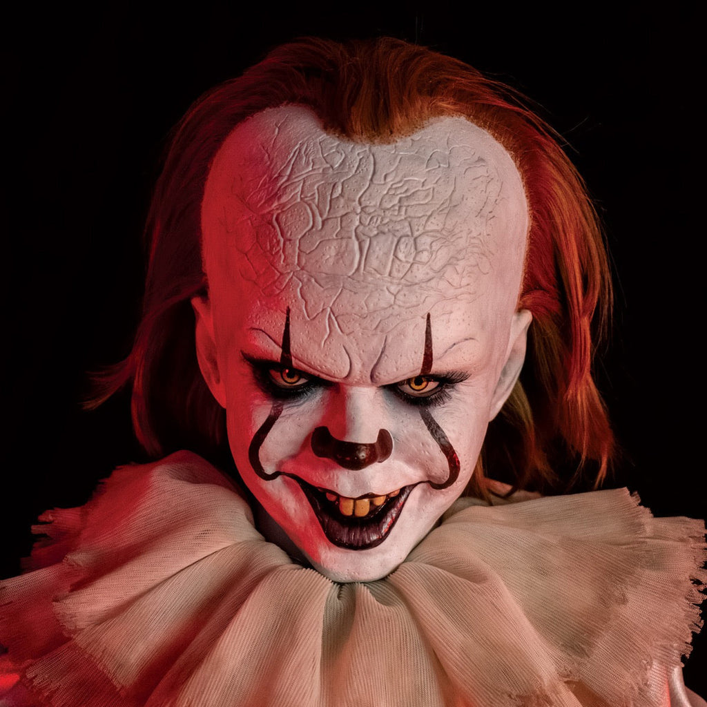 Pennywise doll, close up view under red lighting. clown face, red hair, white skin, large forehead, yellow eyes and nose, dark lips, creepy smile with crooked yellow buck teeth