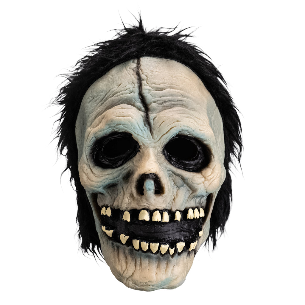 Mask, front view.  White skull-like face.  Black, short shaggy hair, black crack down the forehead. Black rimmed empty eyes, skull like nasal cavity. black, open grinning mouth with several missing teeth