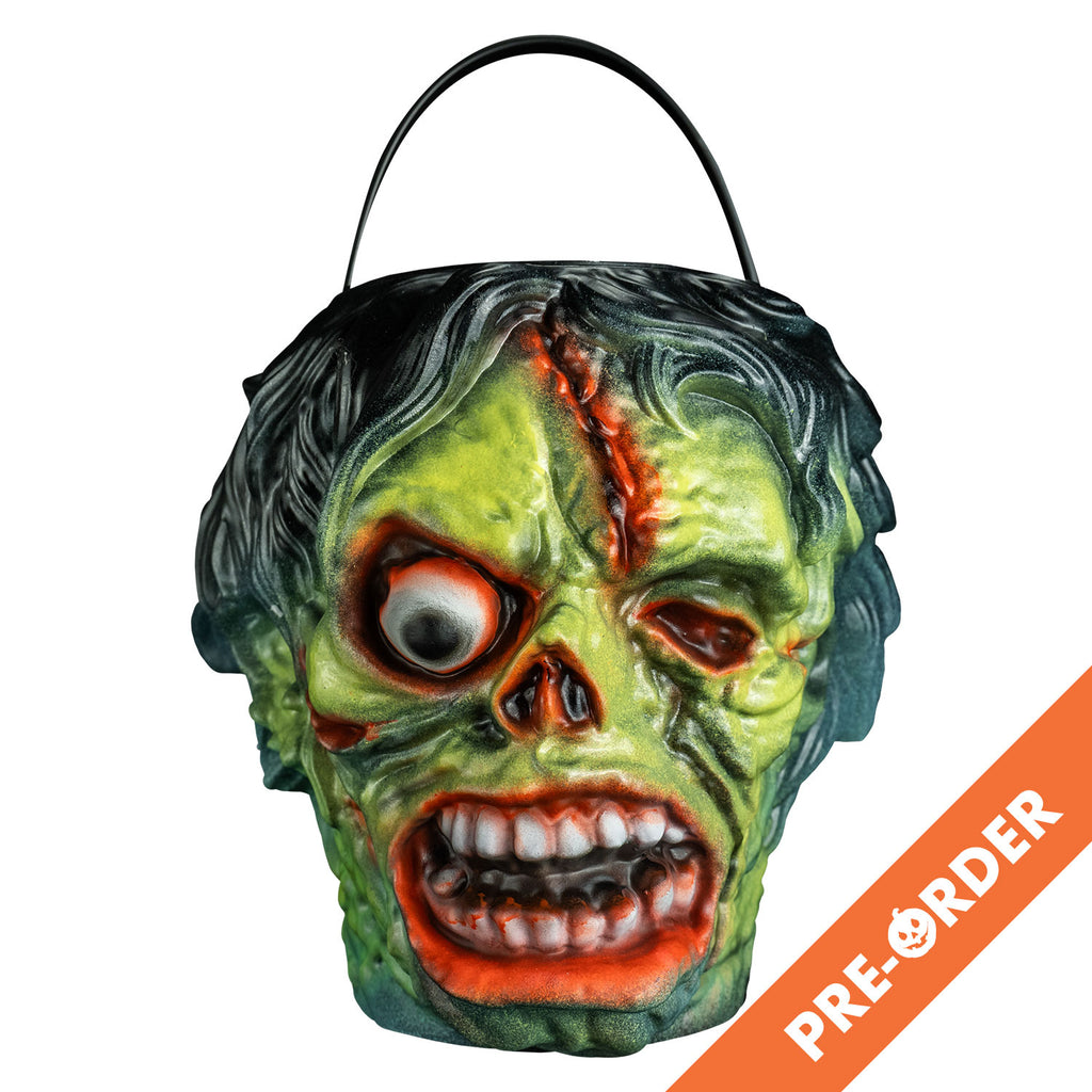 white background, orange diagonal banner at bottom right, white text reads pre-order.  candy pail, front view. Black bushy hair, Green flesh, wrinkled and wounded. Bulging, bloodshot right eye, missing left eye and nose. Open snarling mouth with crooked teeth., black handle at top.