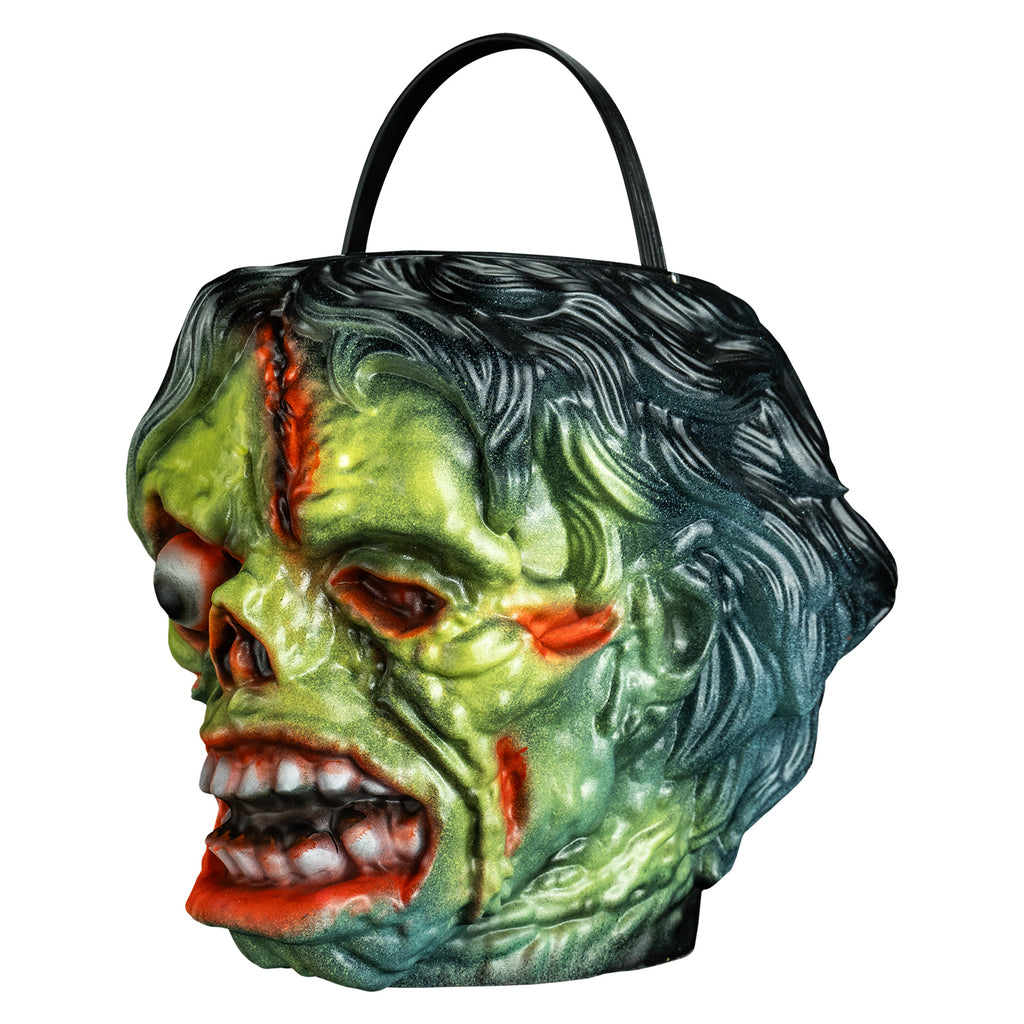 candy pail, left view. Black bushy hair, Green flesh, wrinkled and wounded. Bulging, bloodshot right eye, missing left eye and nose. Open snarling mouth with crooked teeth., black handle at top.