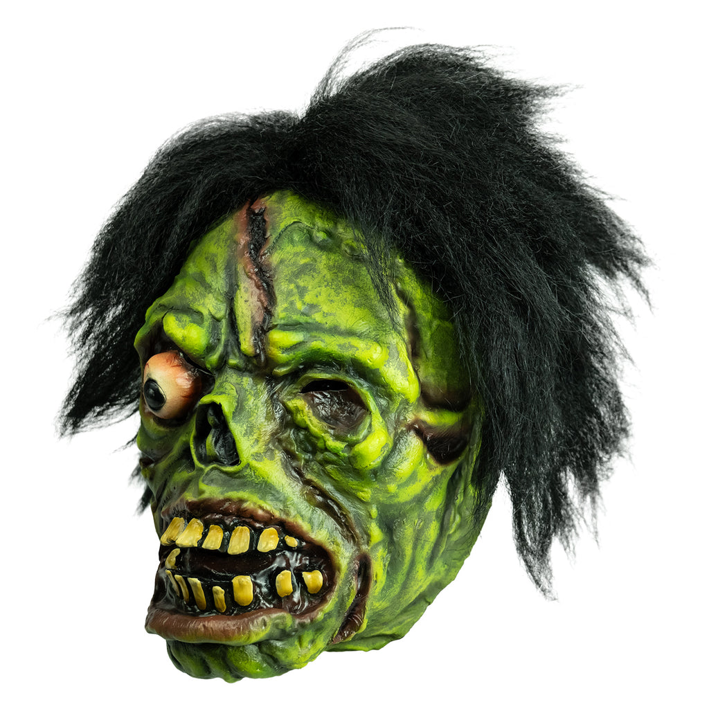 Mask left view. Black bushy hair, Green flesh, wrinkled and wounded. Bulging, bloodshot right eye, missing left eye and nose. Open snarling mouth with yellow crooked teeth.