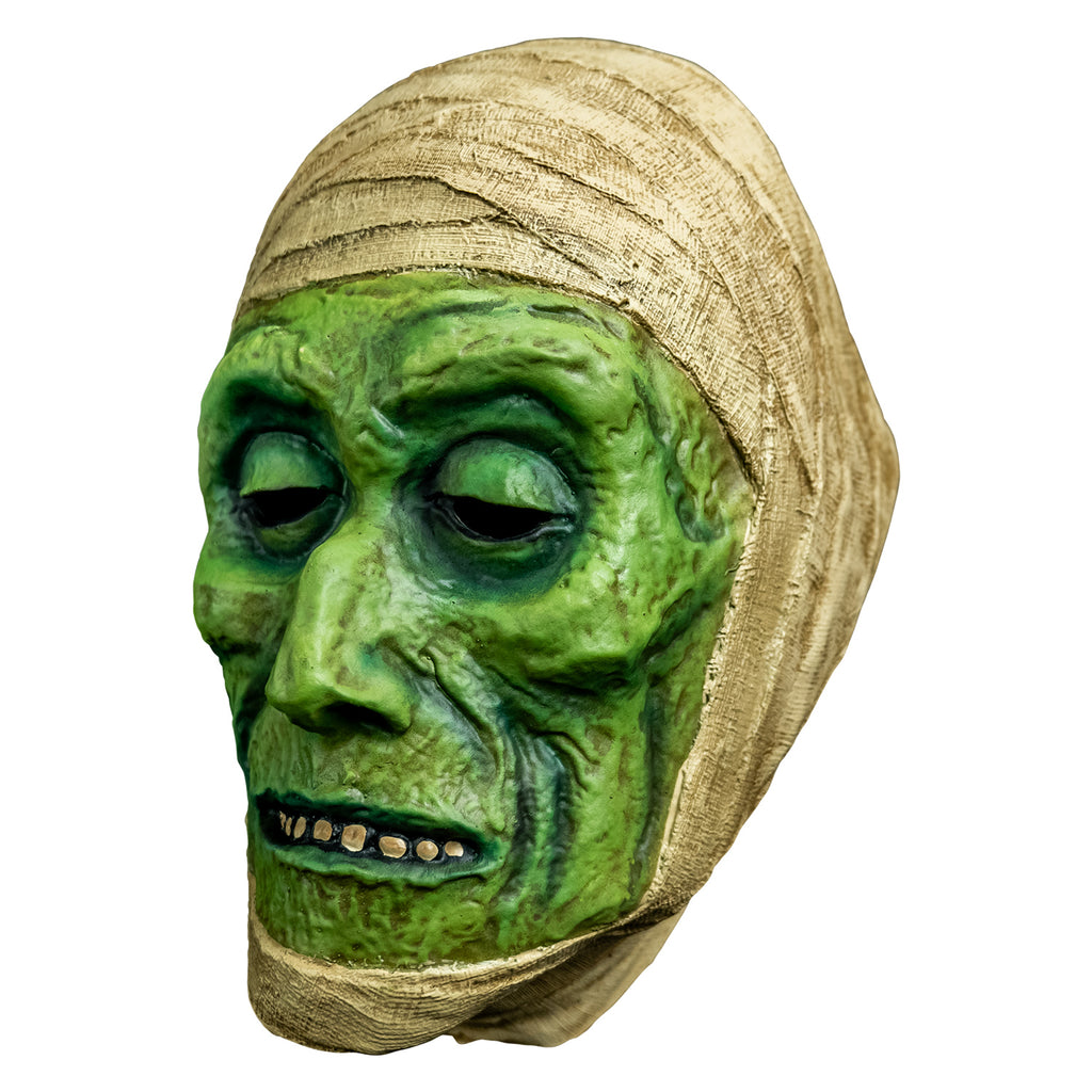 mask, left view. green distressed flesh, eyes slightly closed, mouth with thin lips open showing row of teeth. wrapped in off-white bandages around top of head and perimeter of face.